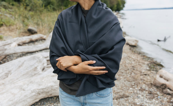 A Large Shepherd's Wool Utility Cloth in Matter Grey wrapped around a person's shoulders and torso at the beach.